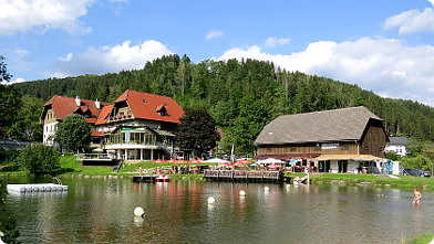 Badesee Mönichwald im Hochsommer mit Seeterrasse und Seegasthof im Hintergrund ...